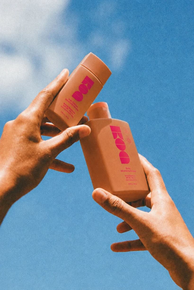 Two hands raising peach-colored bottles against a blue summer sky
